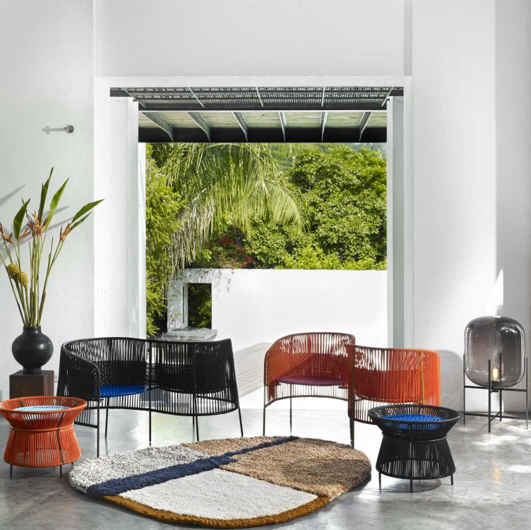 Ames Caribe Basket Table und Outdoor-Möbel-Set mit Stühlen und Teppich in einem hellen Raum.