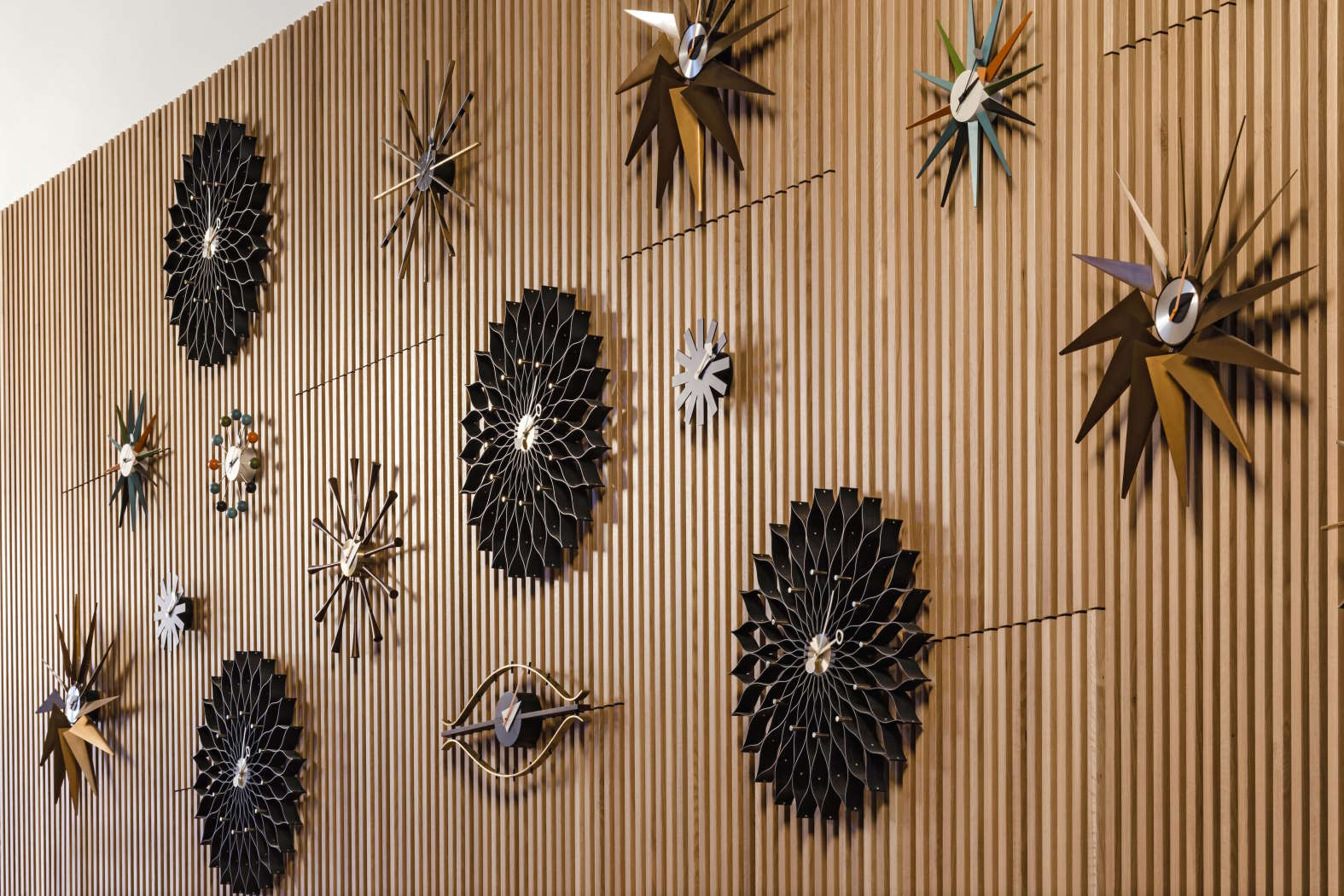 Wand mit verschiedenen Design-Uhren, darunter die Asterisk Clock von Vitra, in unterschiedlichen Formen und Farben.