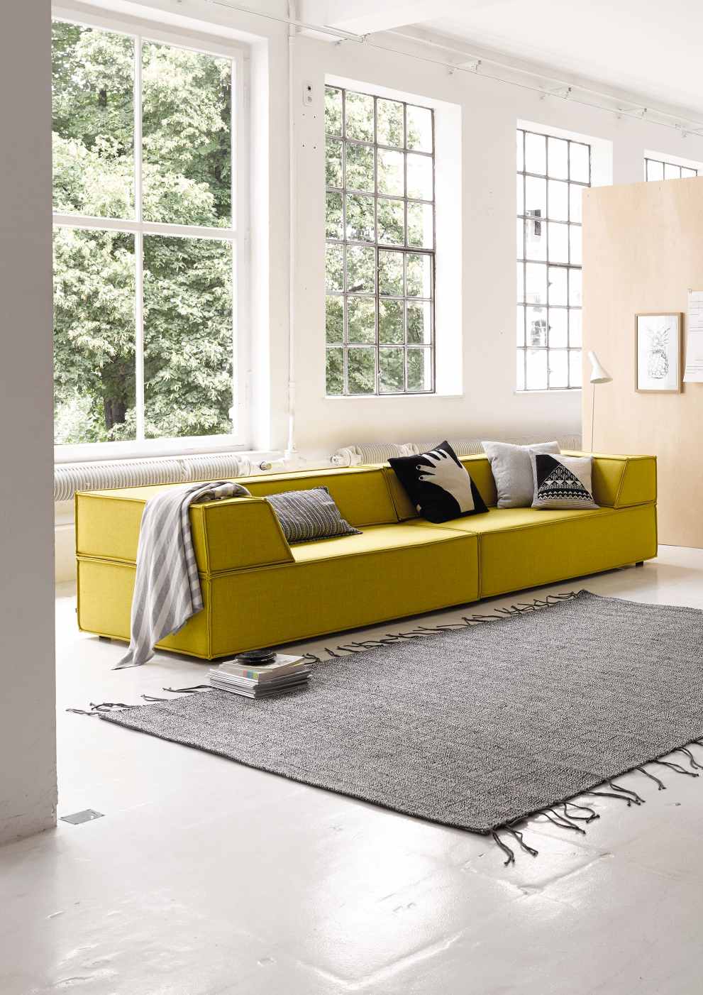 Gelbes Cor Trio Sofa mit Kissen und grauer Decke in modernem Wohnzimmer mit Teppich.
