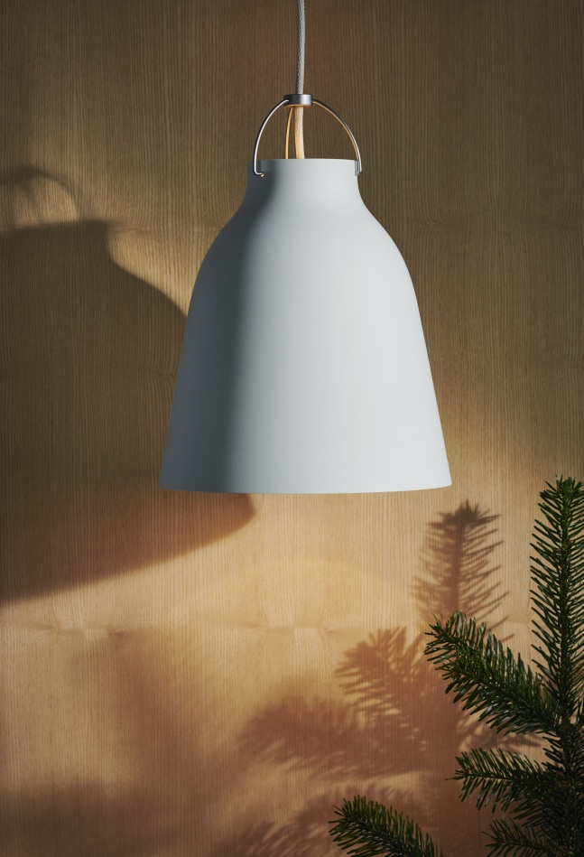 Nahaufnahme der grauen Caravaggio Pendelleuchte von Fritz Hansen vor einer Holzwand mit Tannenzweig.
