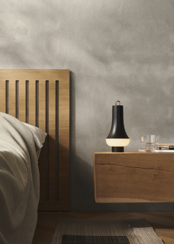 Tomoshi Akkuleuchte in Dunkelbraun auf Nachttisch neben Bett, stimmungsvolle Beleuchtung für Schlafzimmer.