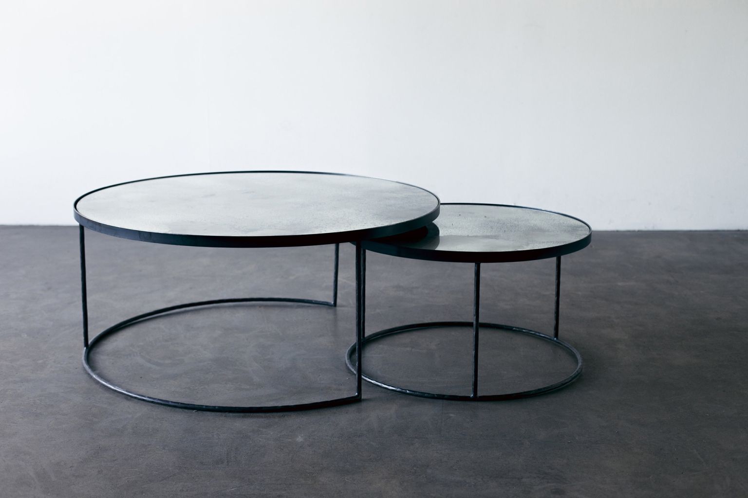 Ethnicraft Couchtisch Set: Zwei runde Beistelltische mit schwarzem Metallgestell und grauer Tischplatte.