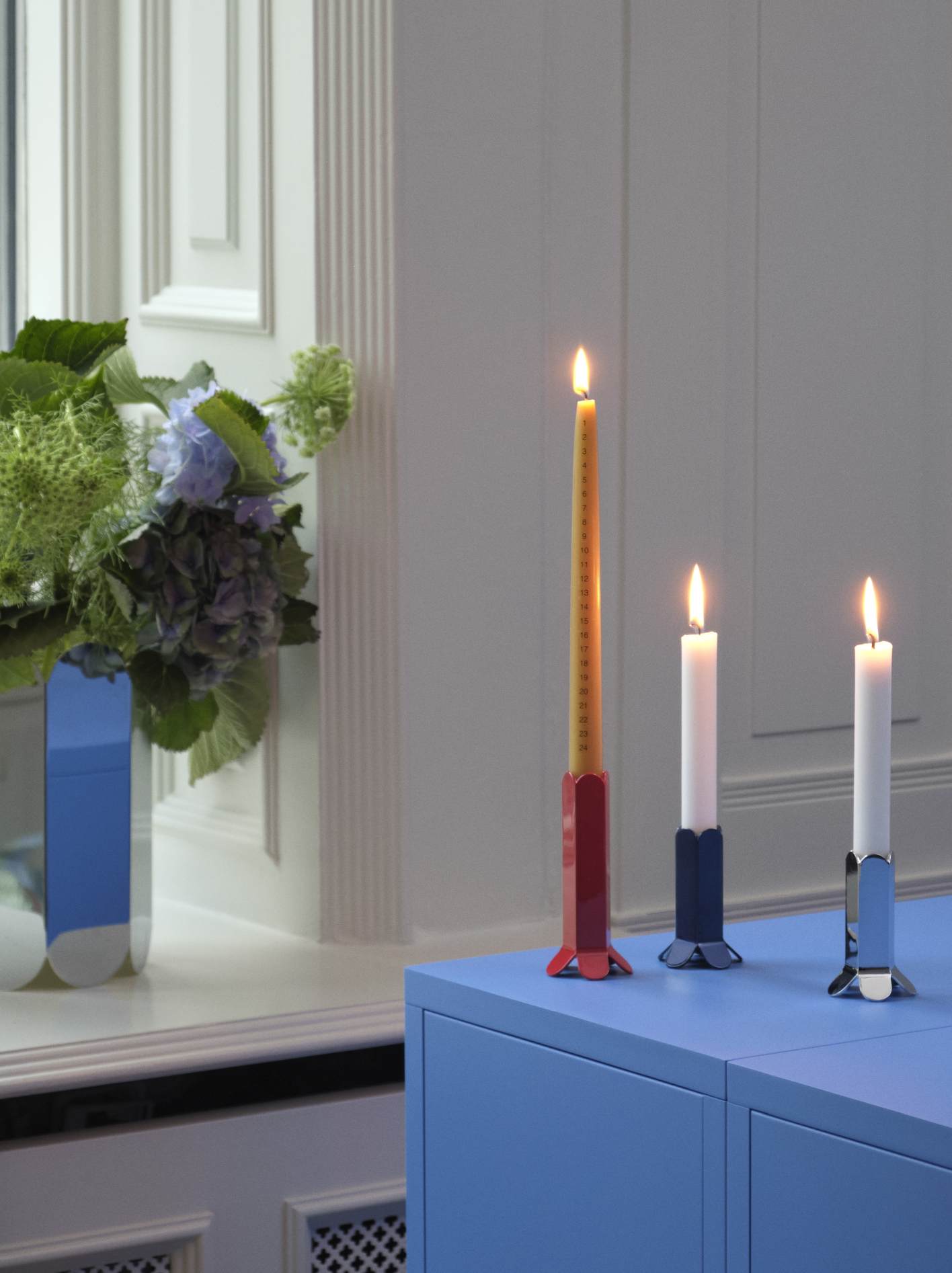 Hay Arcs Vase L Mirror neben Blumenstrauß und farbigen Kerzenhaltern auf blauem Sideboard.