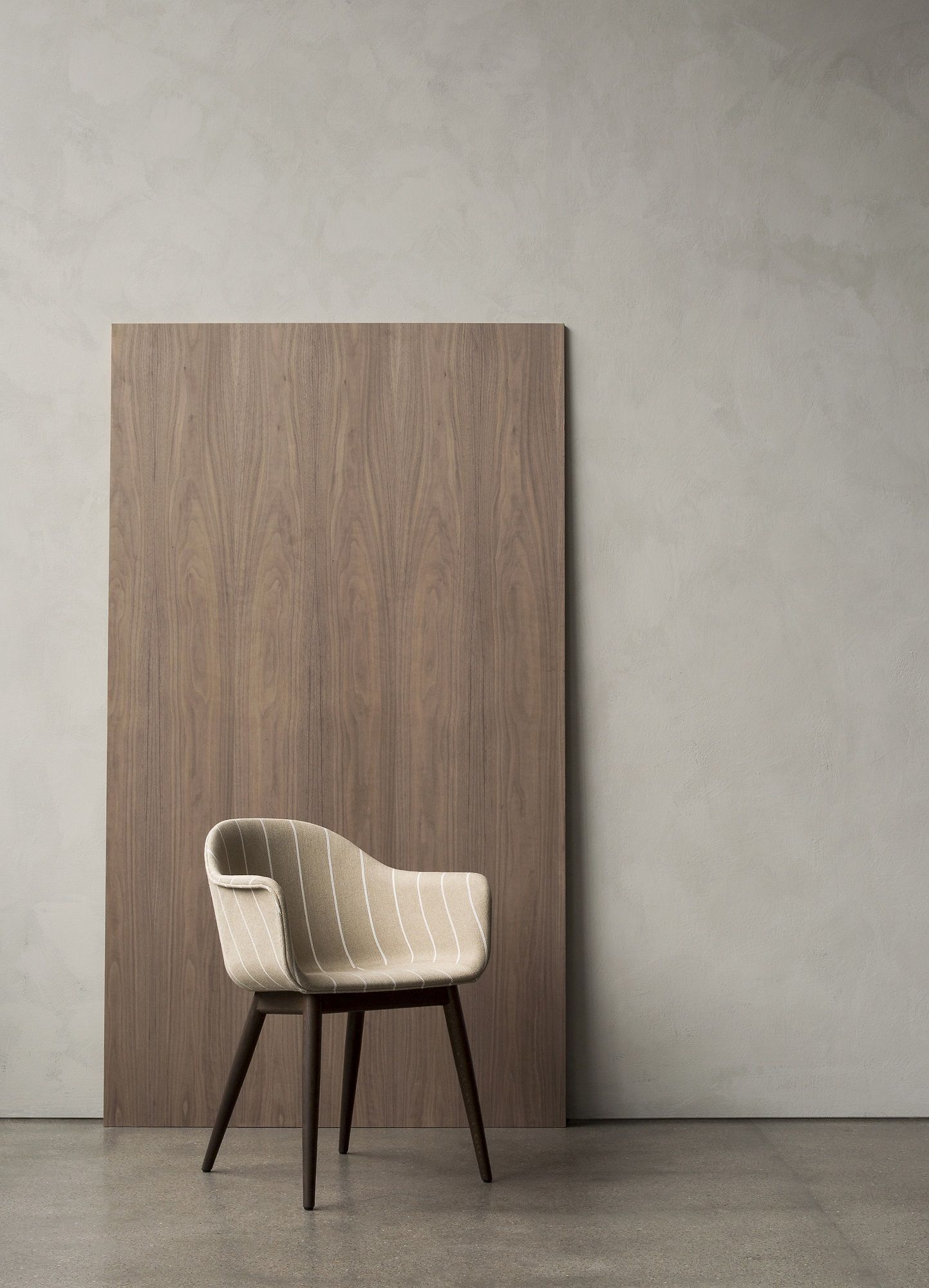 Audo Copenhagen Harbour Dining Chair mit gestreiftem Stoffbezug und dunklen Holzbeinen vor Holzwand.