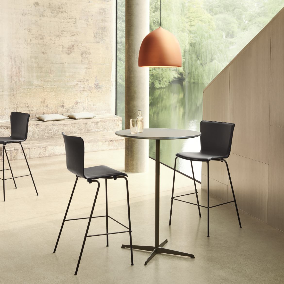 Innenaufnahme mit Fritz Hansen Stehtisch Zirkular, graue Tischplatte, schwarzes Gestell, kombiniert mit Barhockern und Pendelleuchte.