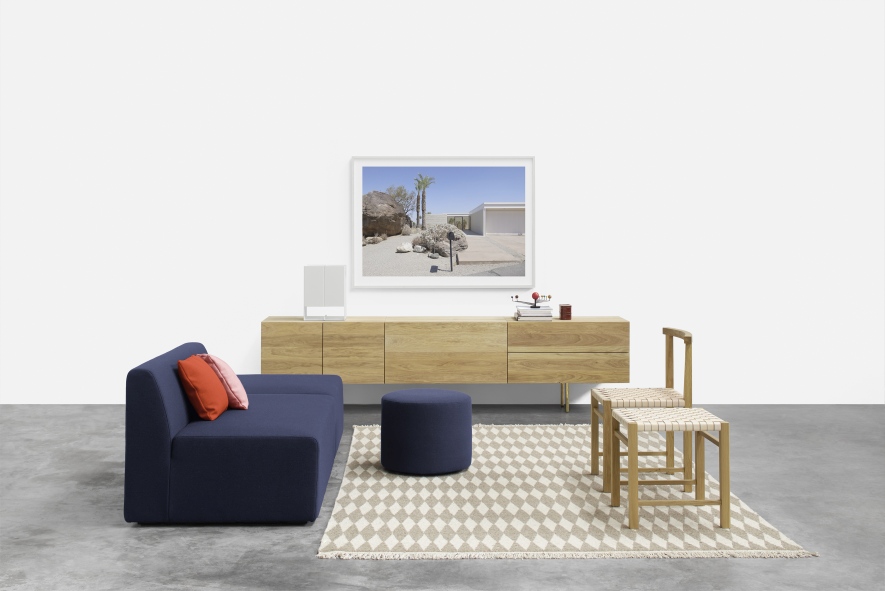 SF06 Kerman Modulsofa von e15 in blau mit Hocker und Holzmöbeln auf Teppich.