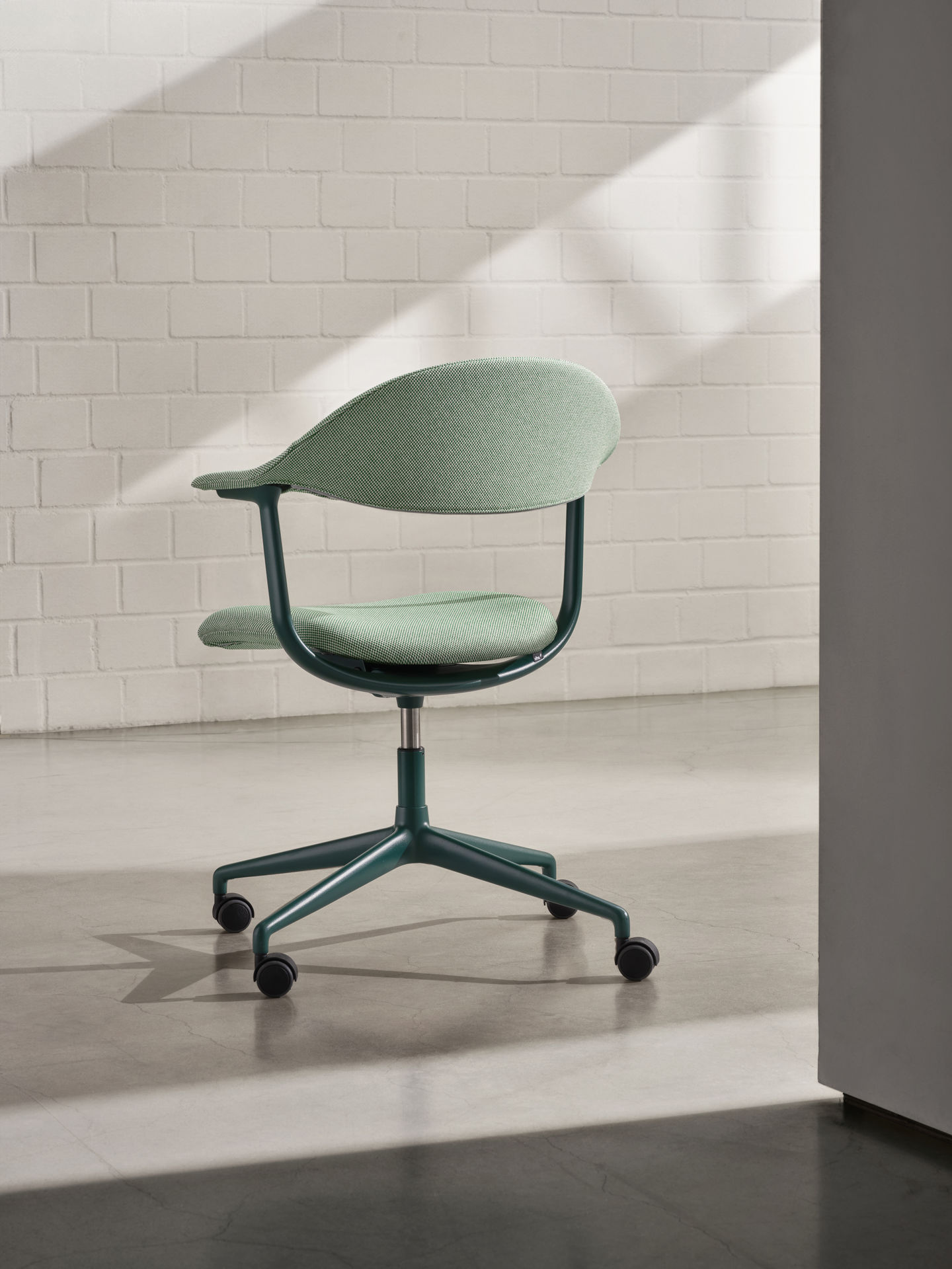 Mynt Bürodrehstuhl von Vitra mit grüner Sitzfläche und Rückenlehne vor einer weißen Ziegelwand.