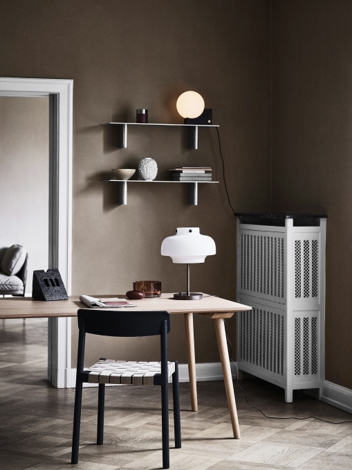 AndTradition In Between Tisch SK5/SK6 aus Eiche mit schwarzem Stuhl und Lampe in braunem Raum.