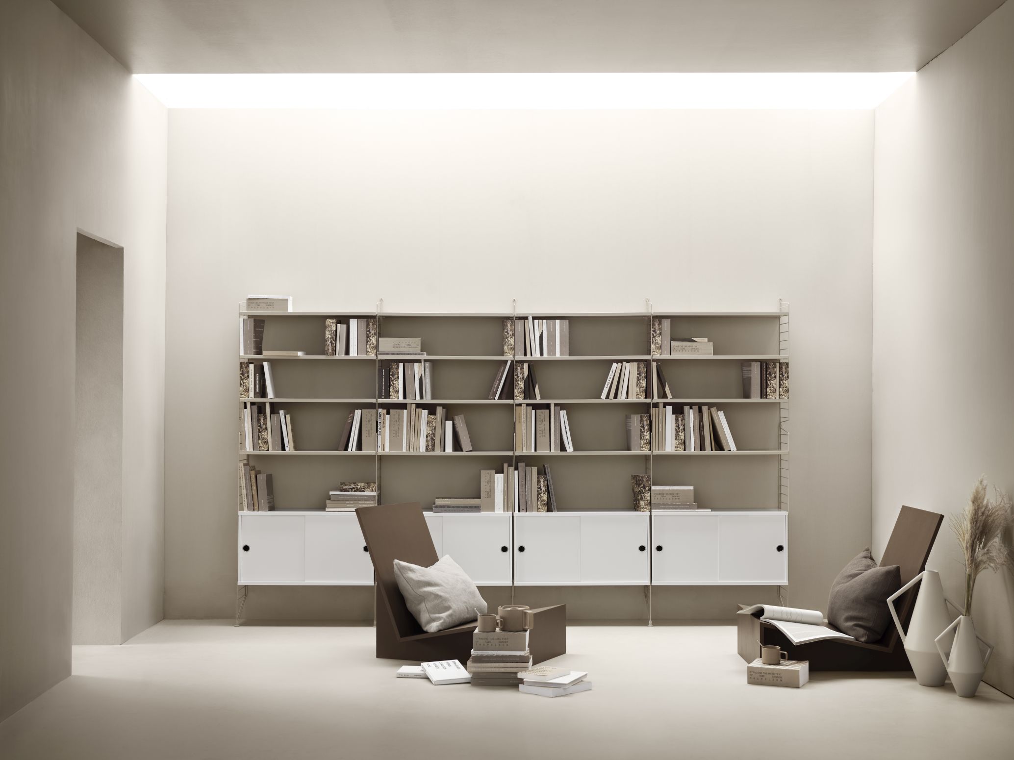 String Regalsystem im Wohnzimmer: Walnussfarbene Regale mit weißen Schränken und minimalistischen Stühlen. Bücher und Dekoration.