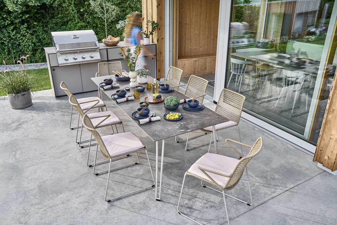 Weishäupl Slope Tisch: Moderner Outdoor Esstisch mit Stühlen auf Terrasse, gedeckt mit Geschirr und Speisen.