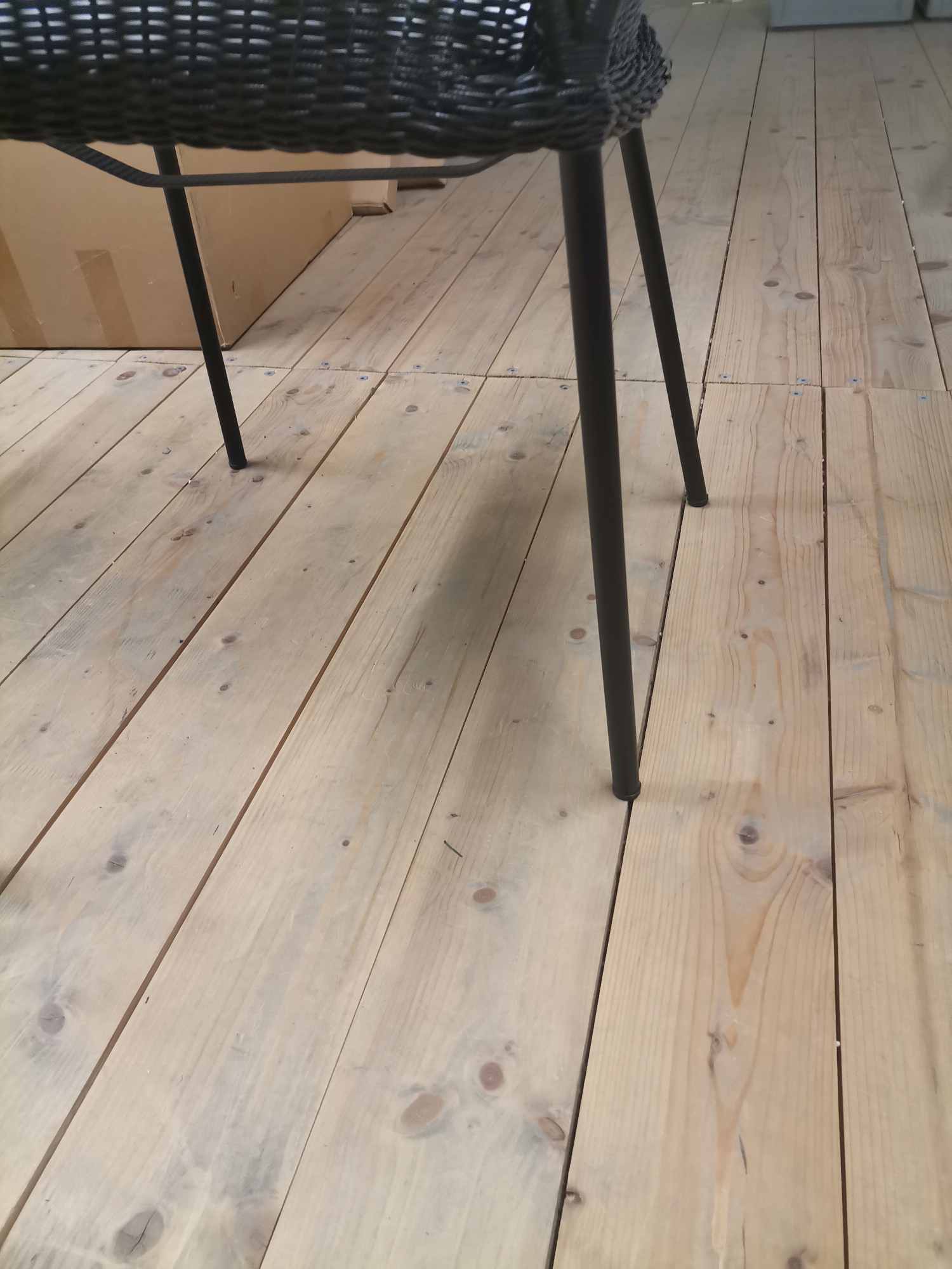 Detailaufnahme des Breeze Outdoor Stuhls mit schwarzem Vierfußgestell auf hellem Holzboden. Cane-Line Gartenmöbel.
