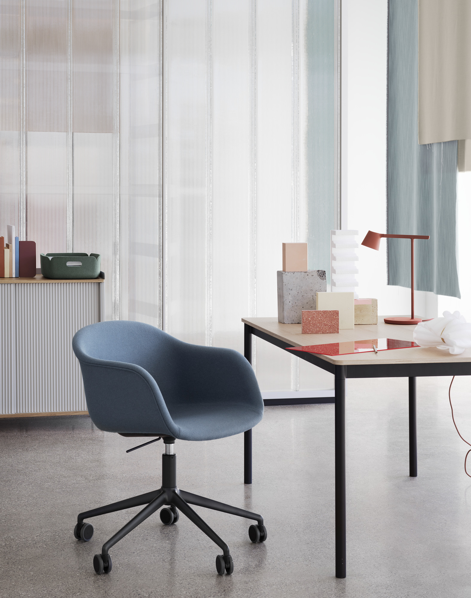 Nahaufnahme des Muuto Base Table Tisches mit schwarzem Gestell und einer blauen Bürostuhl im modernen Büro.