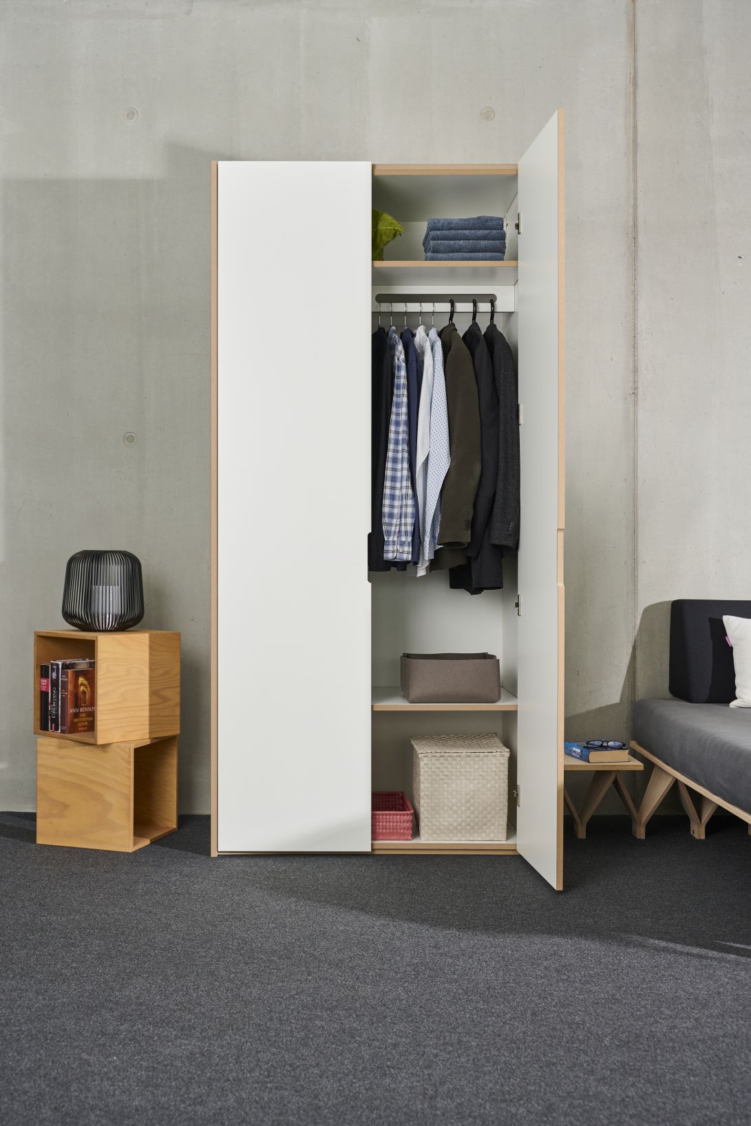 Tojo-Schrank Grundmodul mit offener Tür, Innenraum mit Kleidung, Regalen und Aufbewahrungsboxen.