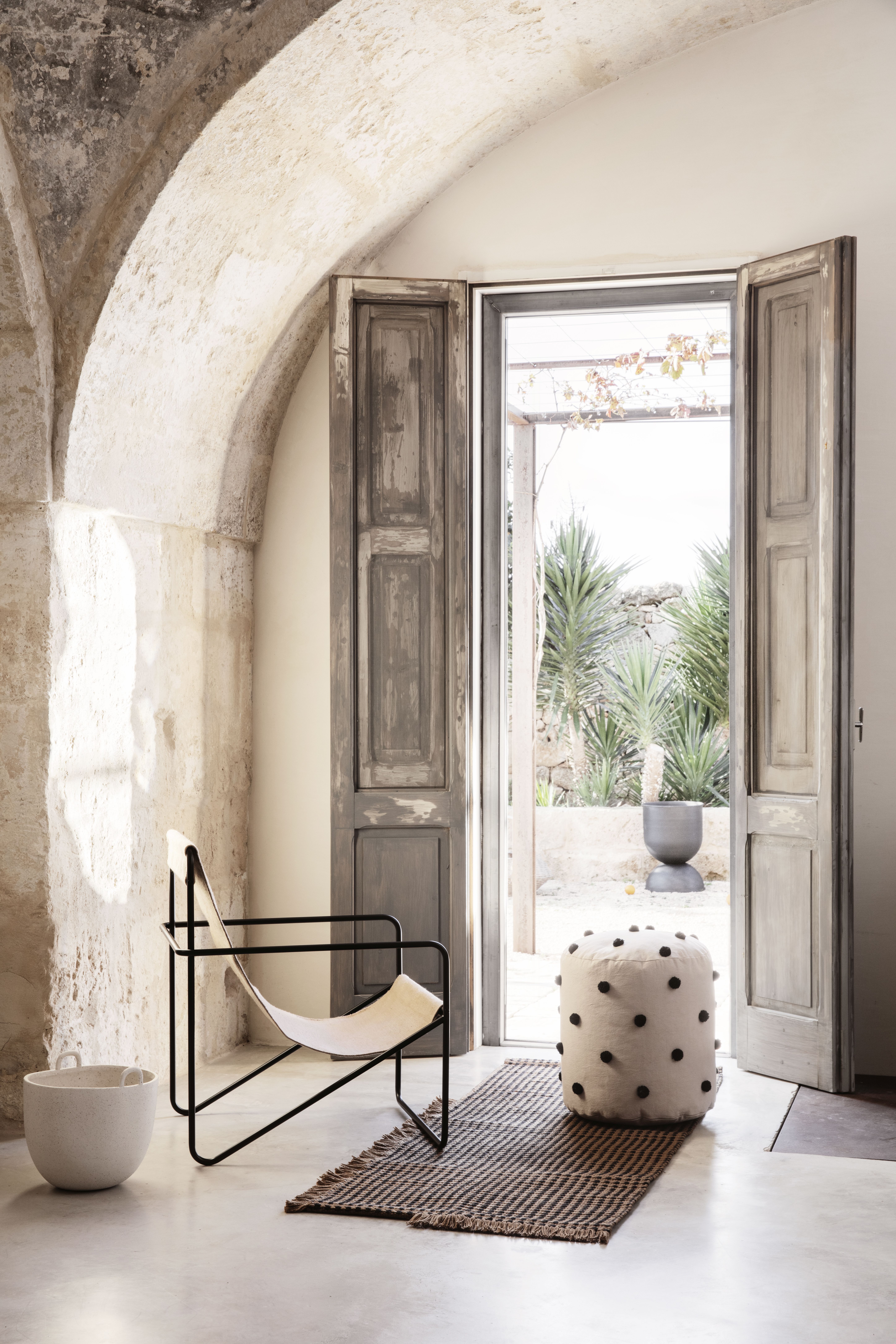 Ferm Living Desert Chair Loungesessel in hellem Raum mit Pouf und Teppich vor geöffneter Tür.