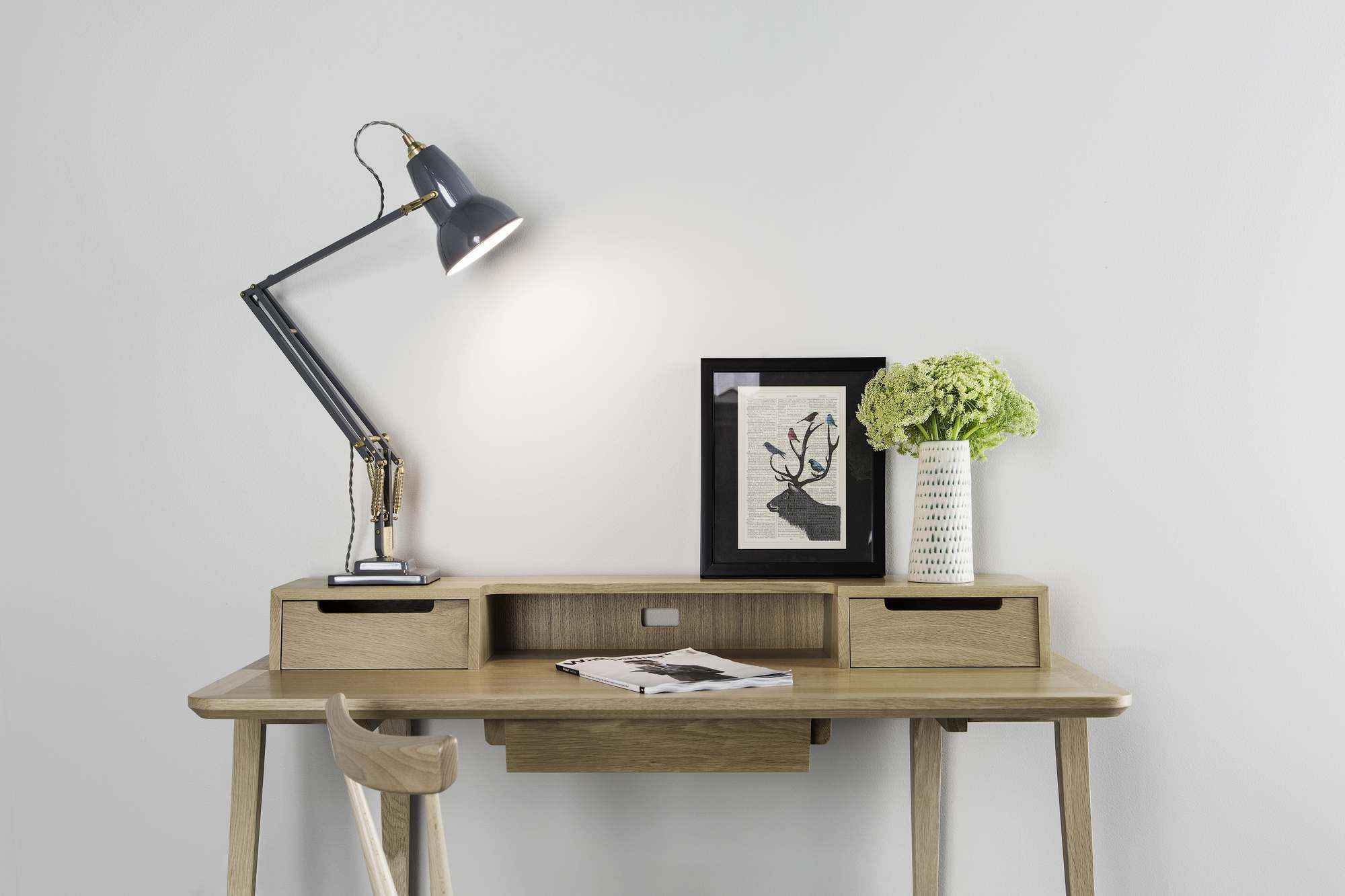Anglepoise Original 1227 Brass Tischleuchte in Grau auf einem Holzschreibtisch mit Dekoration und Stuhl.
