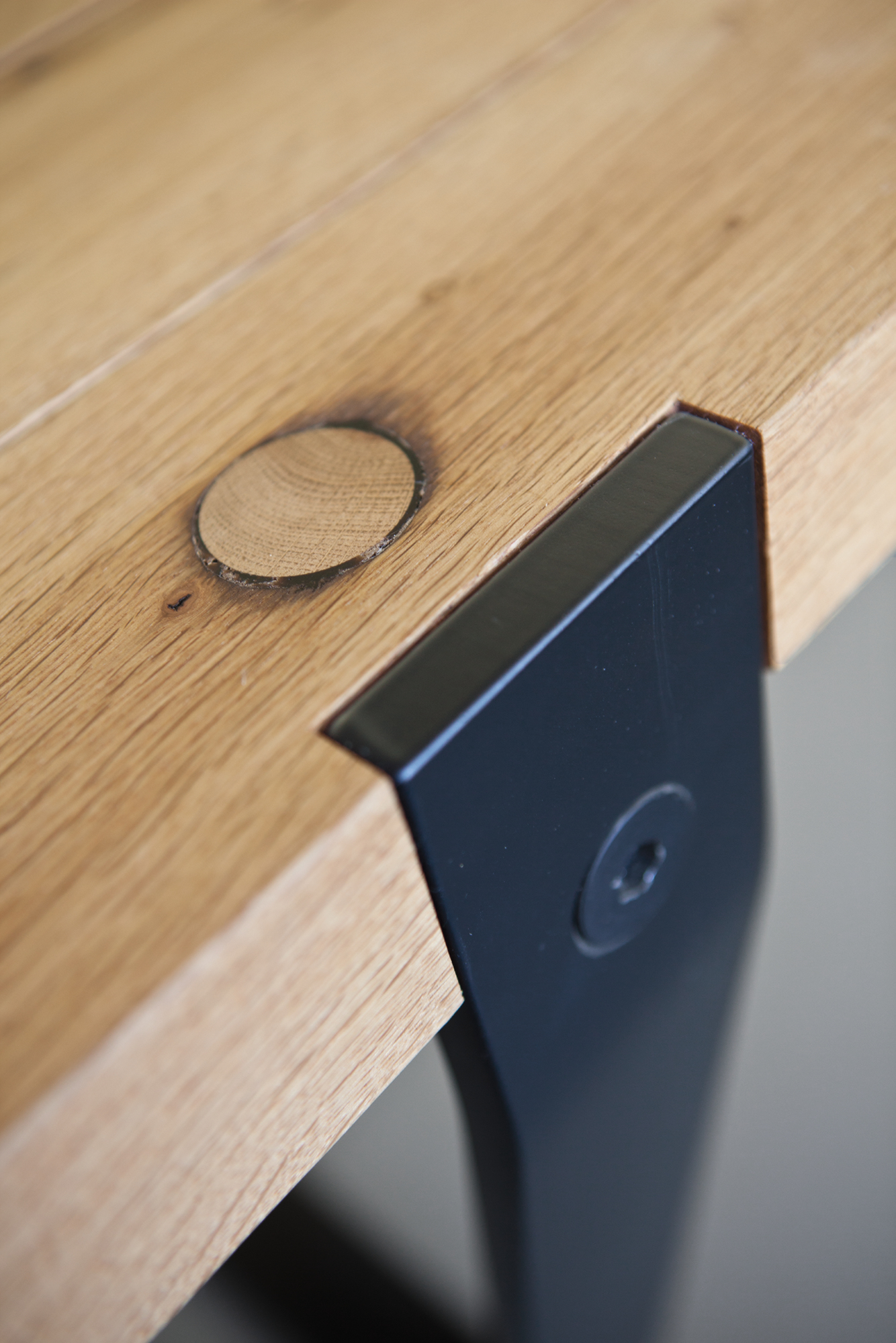 Detailaufnahme Janua BB 11 Clamp Tisch Nussbaum, Tischplatte aus Massivholz mit schwarzer Metallklammer.