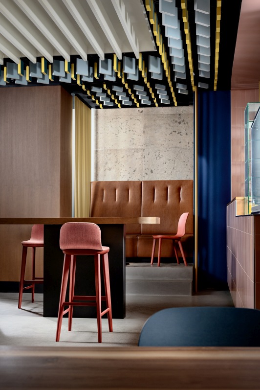 Aeon Barstool Barhocker in Rot vor einer Bar mit brauner Sitzbank und modernem Deckendesign.