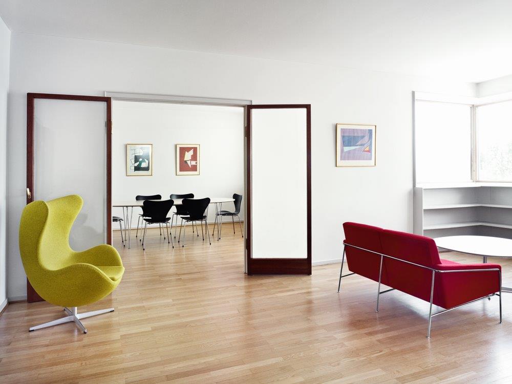 Gelber Egg Chair Sessel von Fritz Hansen in modernem Wohnzimmer mit rotem Sofa und Esstisch.