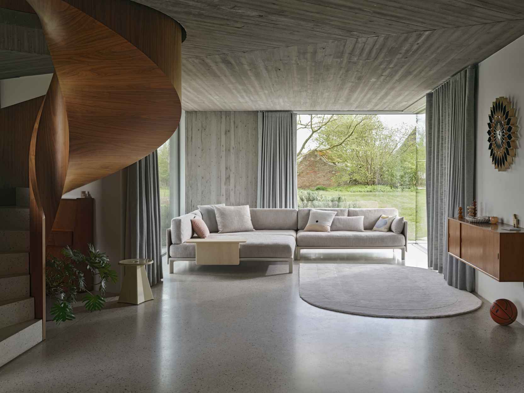 Helles Wohnzimmer mit großem Ecksofa und Vitra Anagram Panel als Ablagefläche, spiralförmige Holztreppe im Hintergrund.
