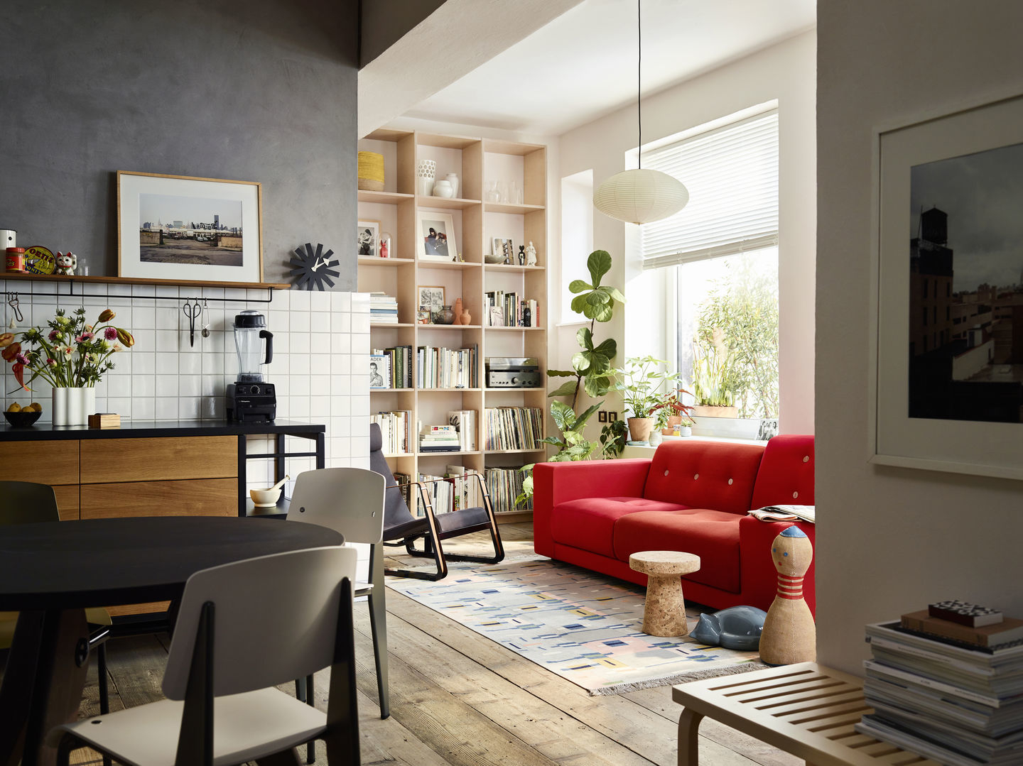 Helle Wohnungseinrichtung mit Vitra Stühlen am Esstisch, rotem Sofa und großem Bücherregal im Hintergrund.