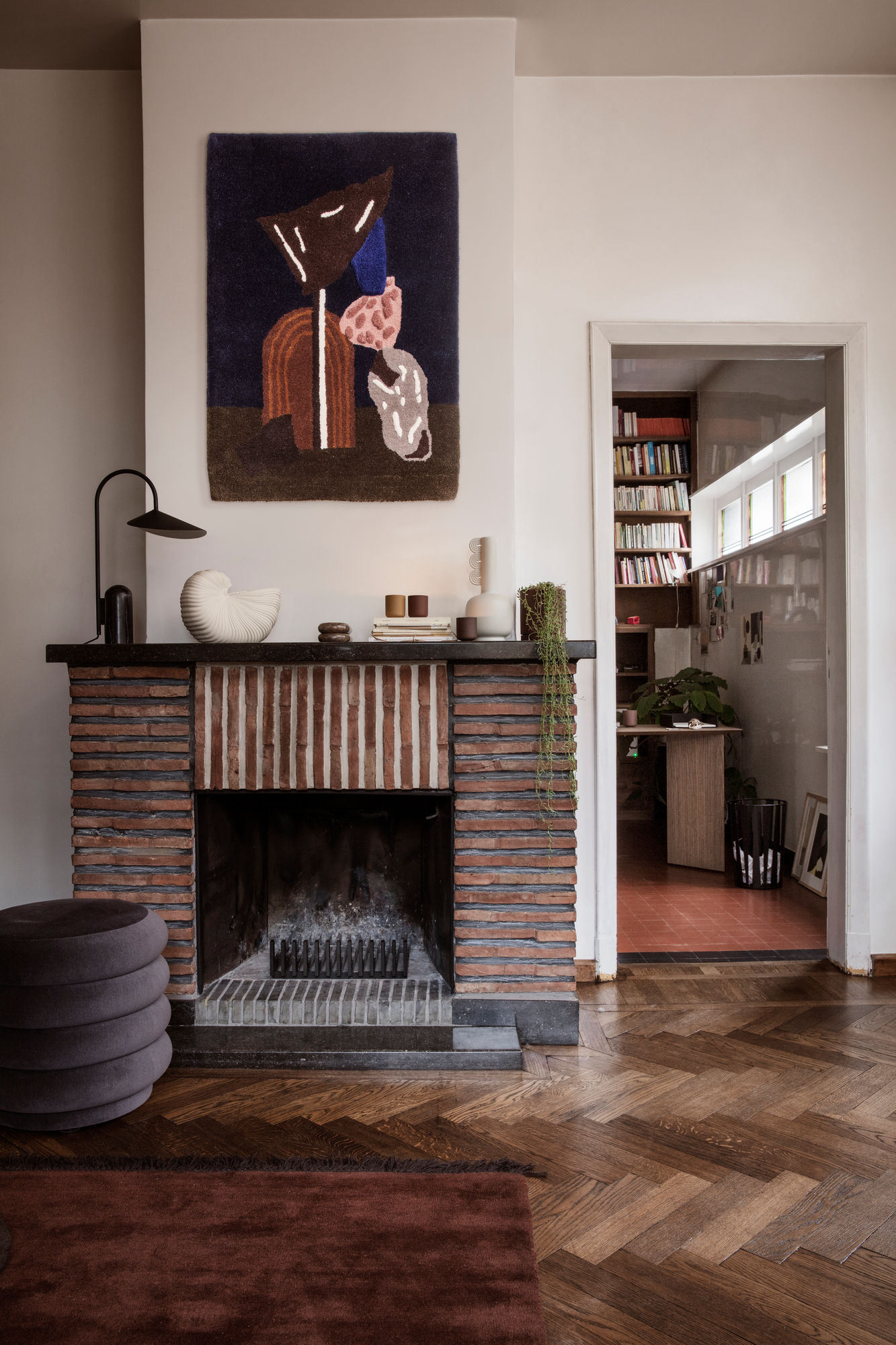 Dekoratives Wohnzimmer mit Kamin, Shell Pot Vase von Ferm Living und abstrakten Wandteppich für stilvolles Interieur.