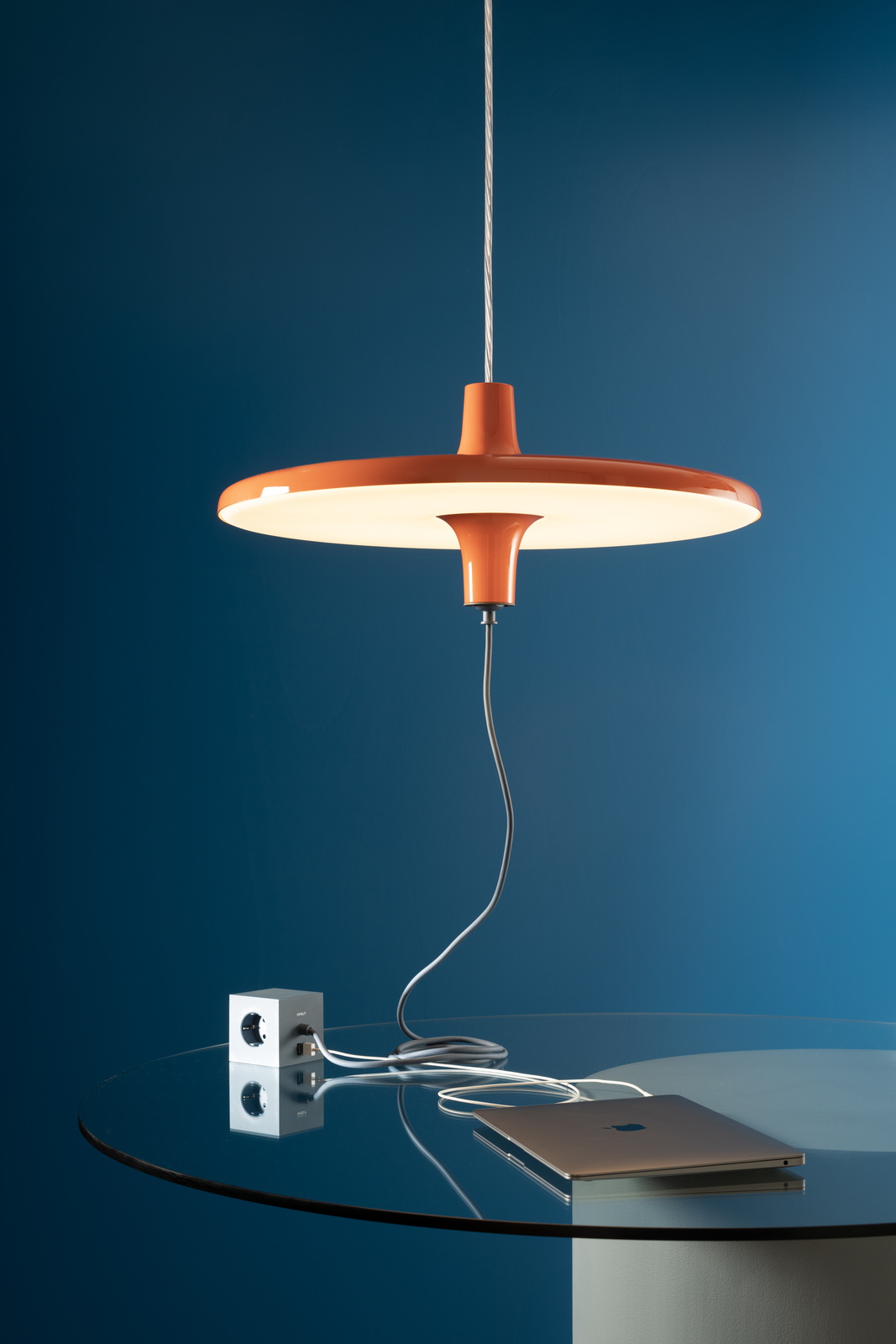 Orange Avro Hängeleuchte von Martinelli Luce über einem Glastisch mit Laptop und Steckerwürfel.