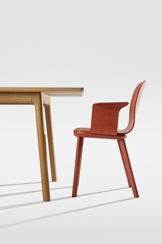 Aeon Comfort Chair Armlehnstuhl Zeitraum in Rot neben einem Holztisch auf weißem Hintergrund.