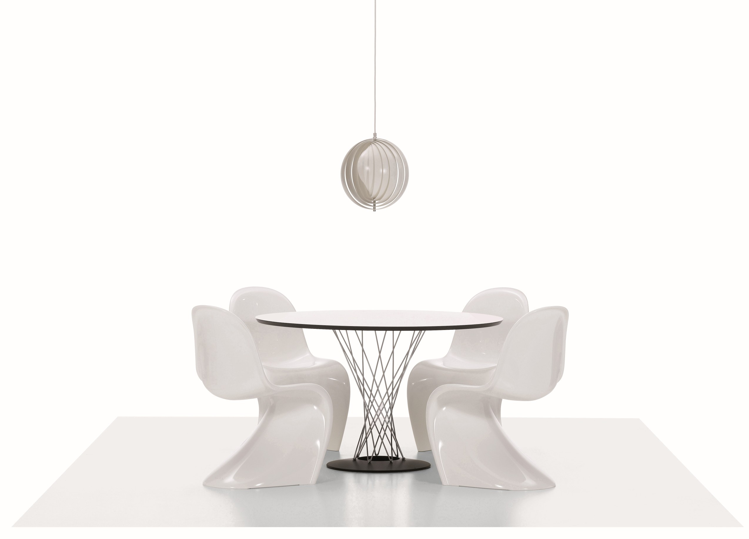 Vier weiße Panton Stühle um einen runden Tisch mit Drahtgestell und Lampe.
