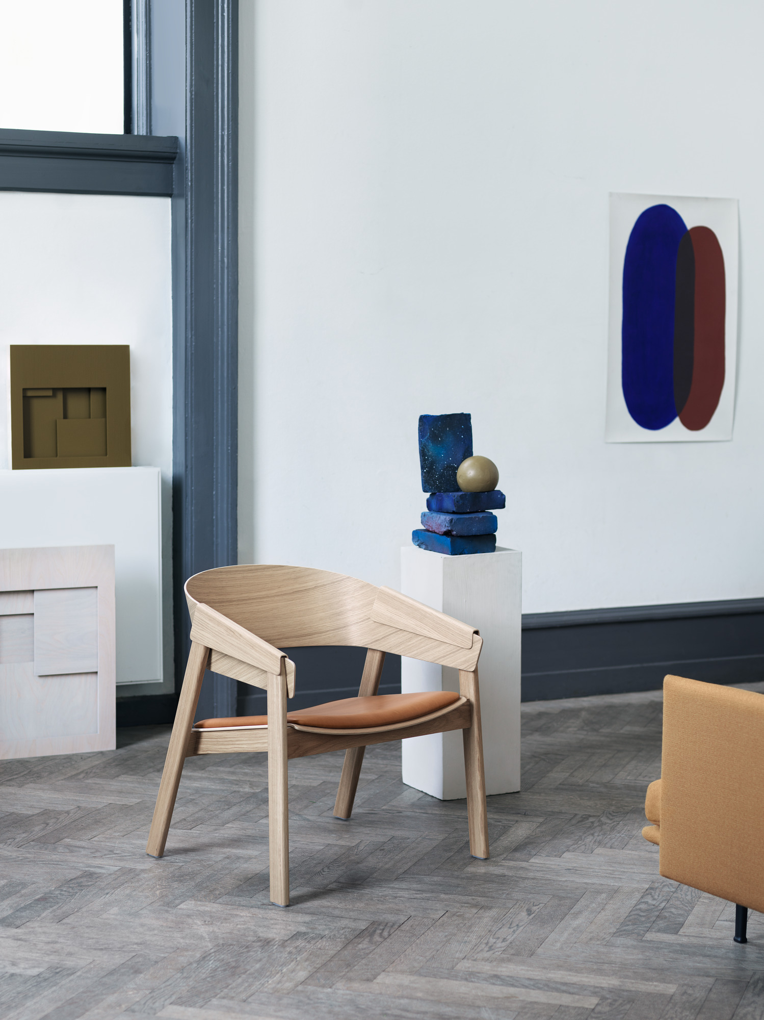 Muuto Cover Lounge Chair Stuhl aus hellem Holz mit braunem Ledersitz in modernem Ambiente.