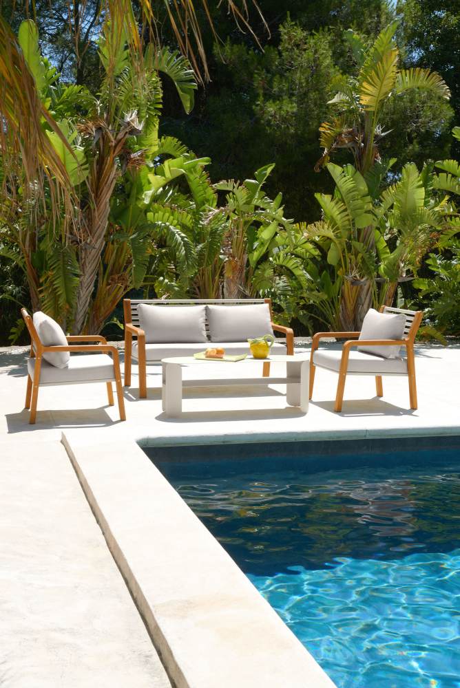 Somerset Sessel und Outdoor-Lounge-Möbel von Fermob neben einem Pool mit tropischen Pflanzen im Hintergrund.