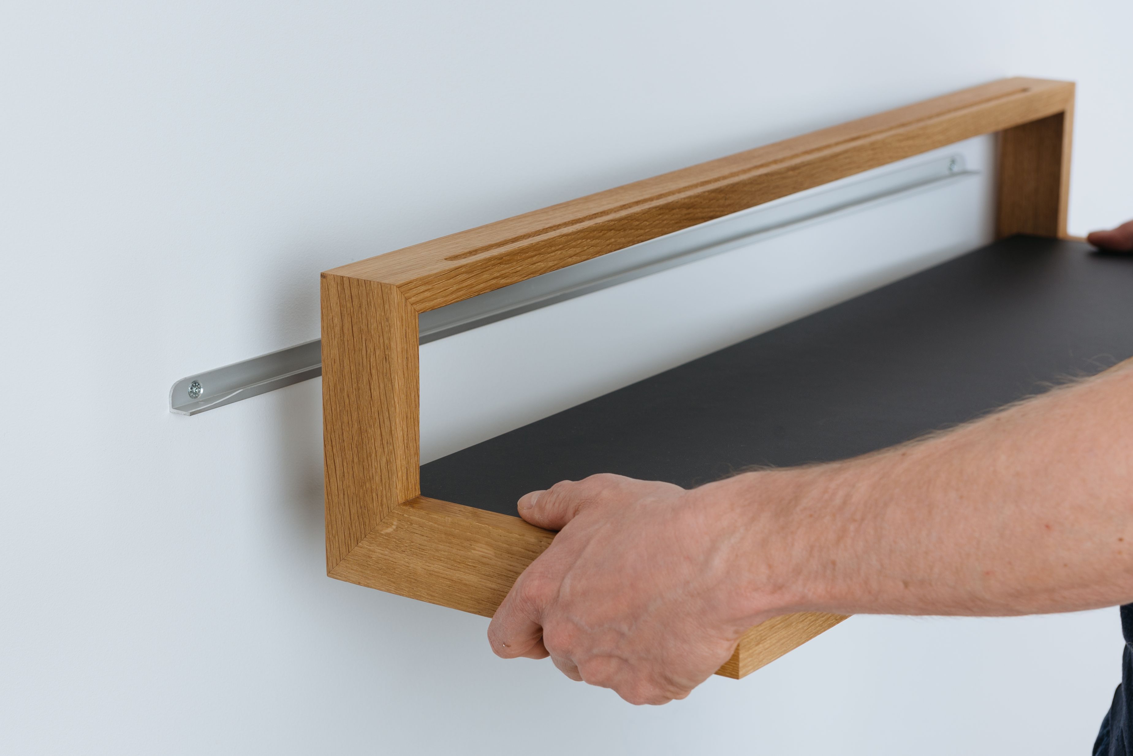 Ablageboard buck das kleine b wird an einer weißen Wand montiert. Holzrahmen mit schwarzer Ablagefläche.
