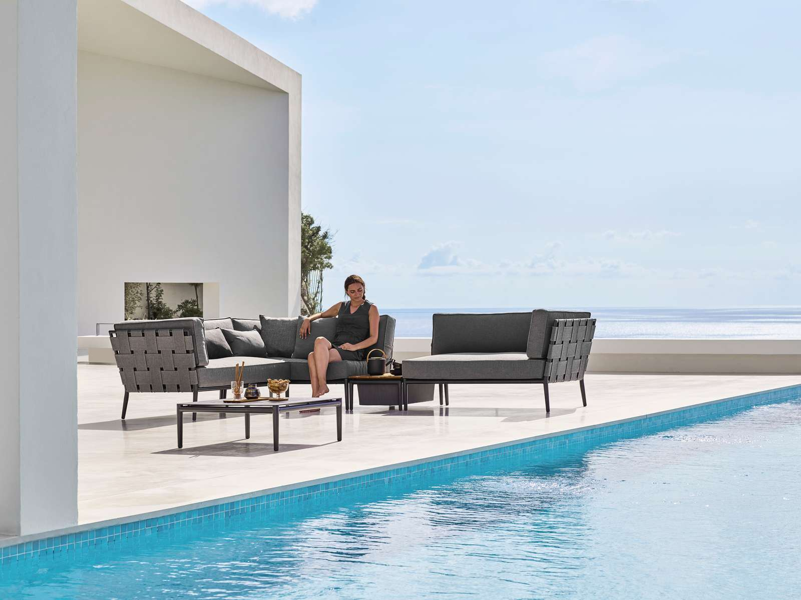 Frau entspannt auf Cane-Line Conic Outdoor Modulsofa rechts, graues Lounge-Set am Pool.