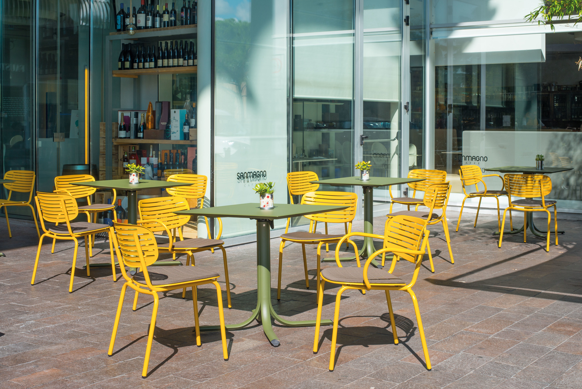 Gelbe Mom Stühle von Emu mit olivgrünen Tischen im Außenbereich eines Cafés.