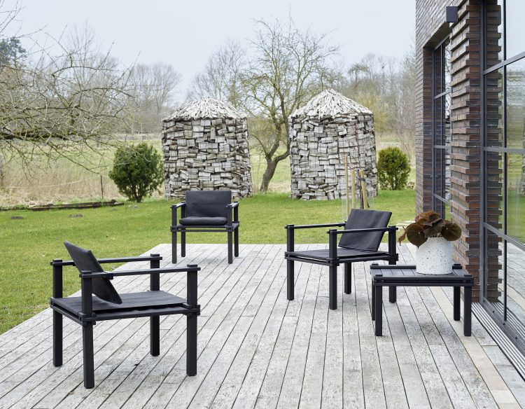 Drei schwarze Farmer Sessel Outdoor Cor und ein Beistelltisch auf einer Holzterrasse im Garten.