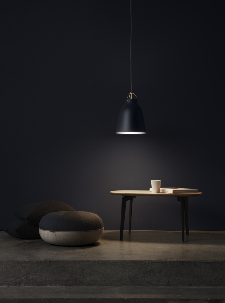 Schwarze Caravaggio Pendelleuchte von Fritz Hansen über kleinem Tisch mit Buch und Tasse in dunklem Raum.