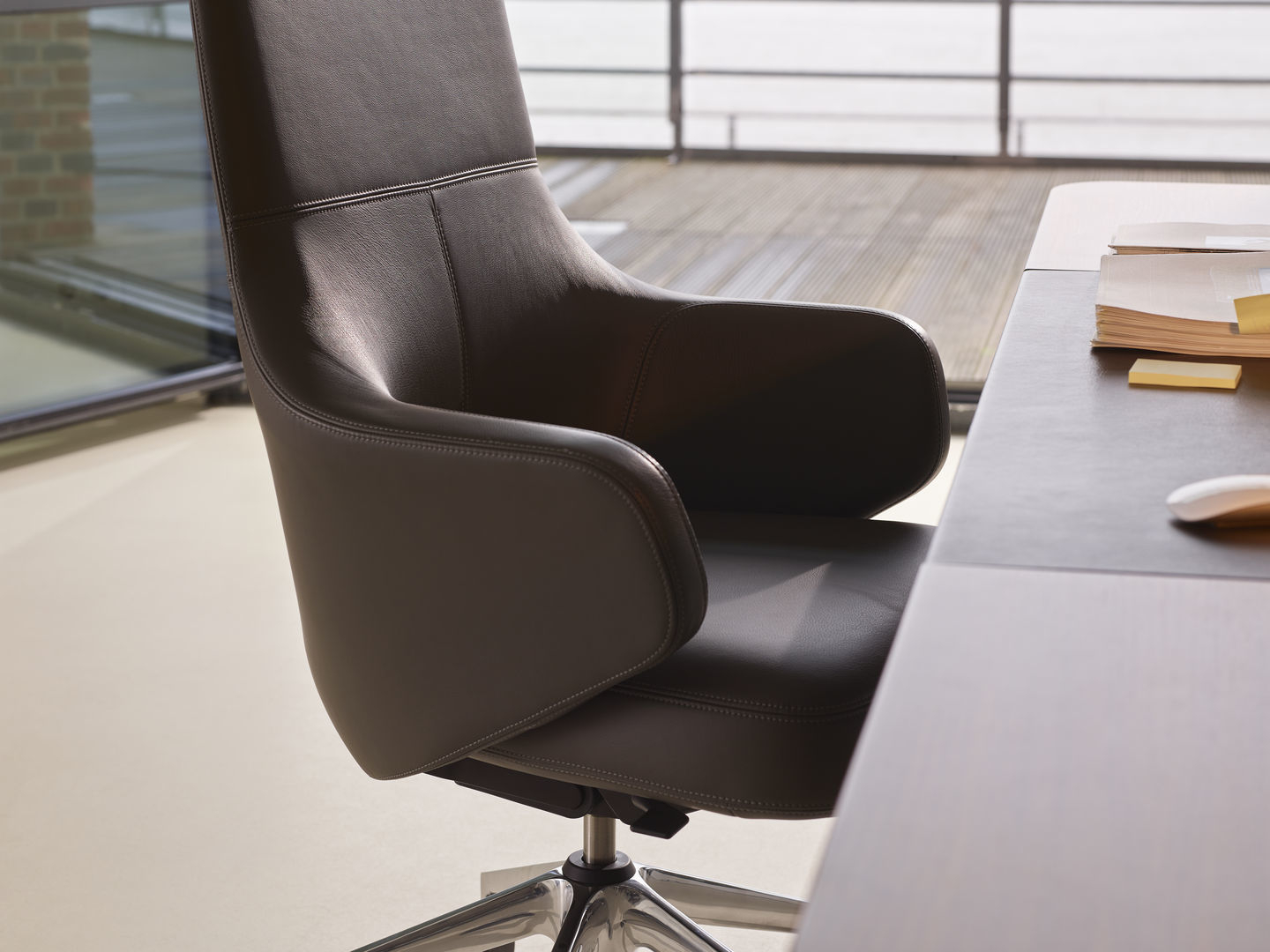 Detailaufnahme des Grand Executive Highback Konferenzstuhls von Vitra mit braunem Lederbezug und Aluminiumfußkreuz.