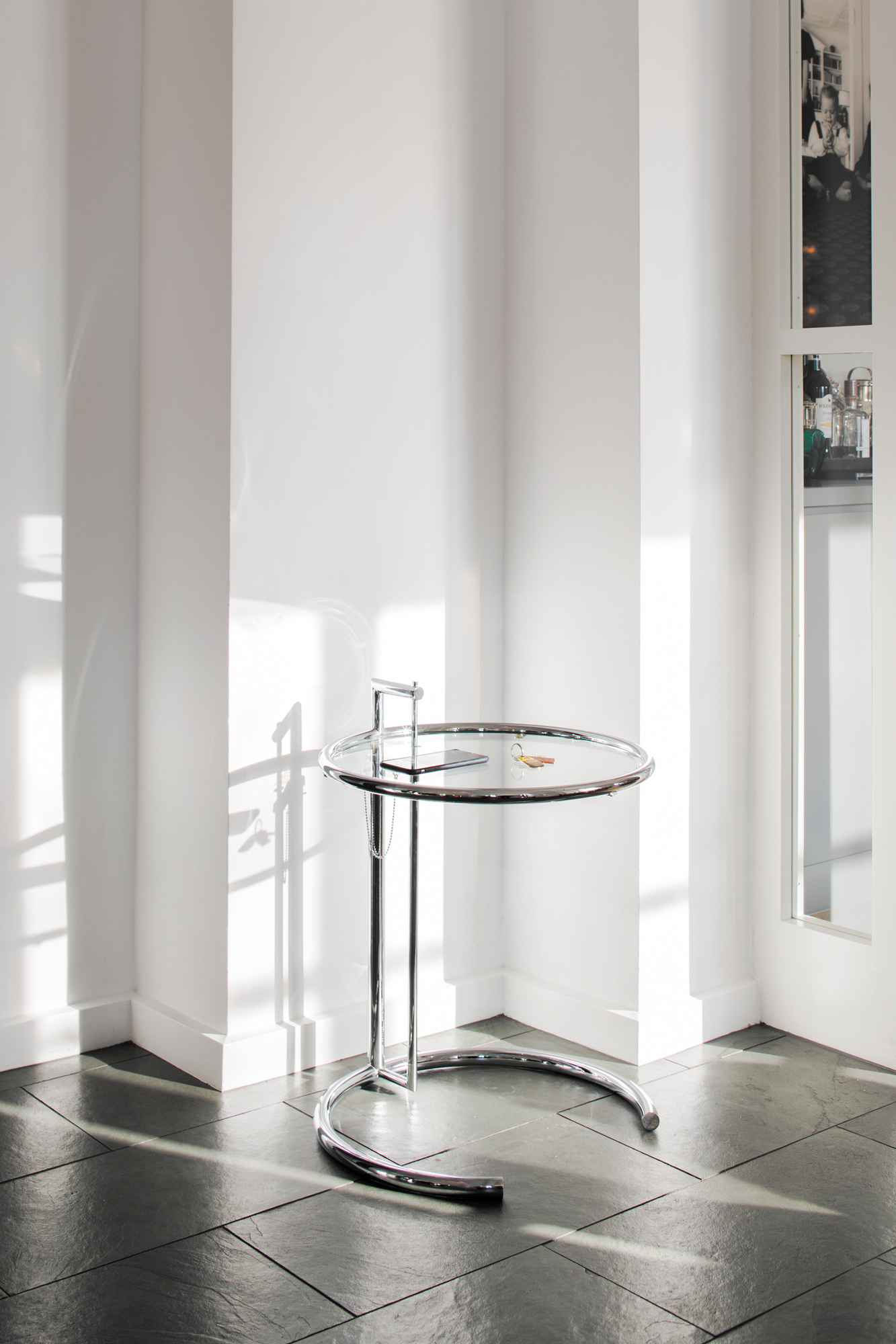 ClassiCon Adjustable Table E1027 Beistelltisch mit Glasplatte und verchromtem Stahlrohrgestell im hellen Raum.