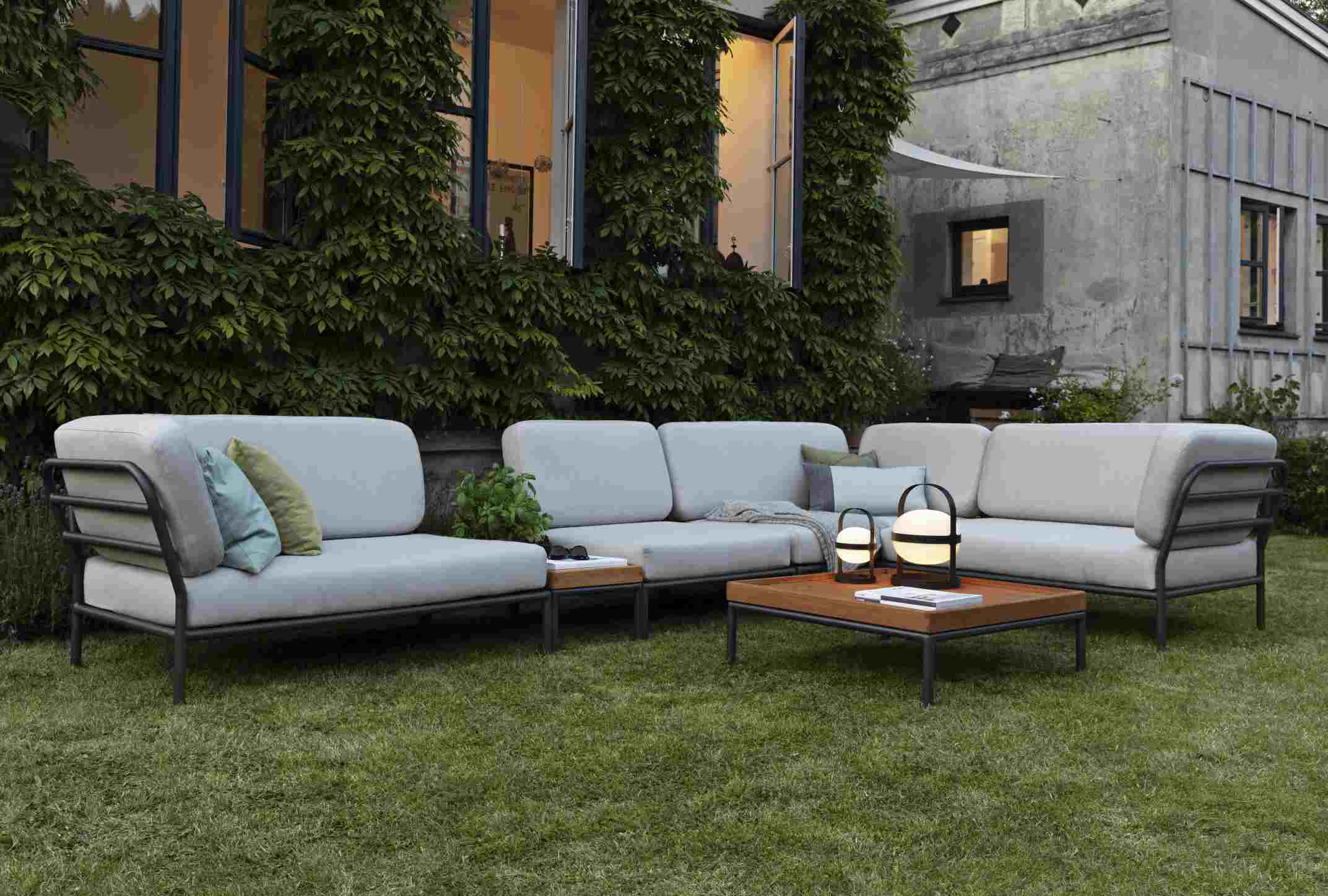 Houe Level Outdoor Lounge Sofa mit Couchtisch und Gartenbeleuchtung auf einer grünen Rasenfläche.