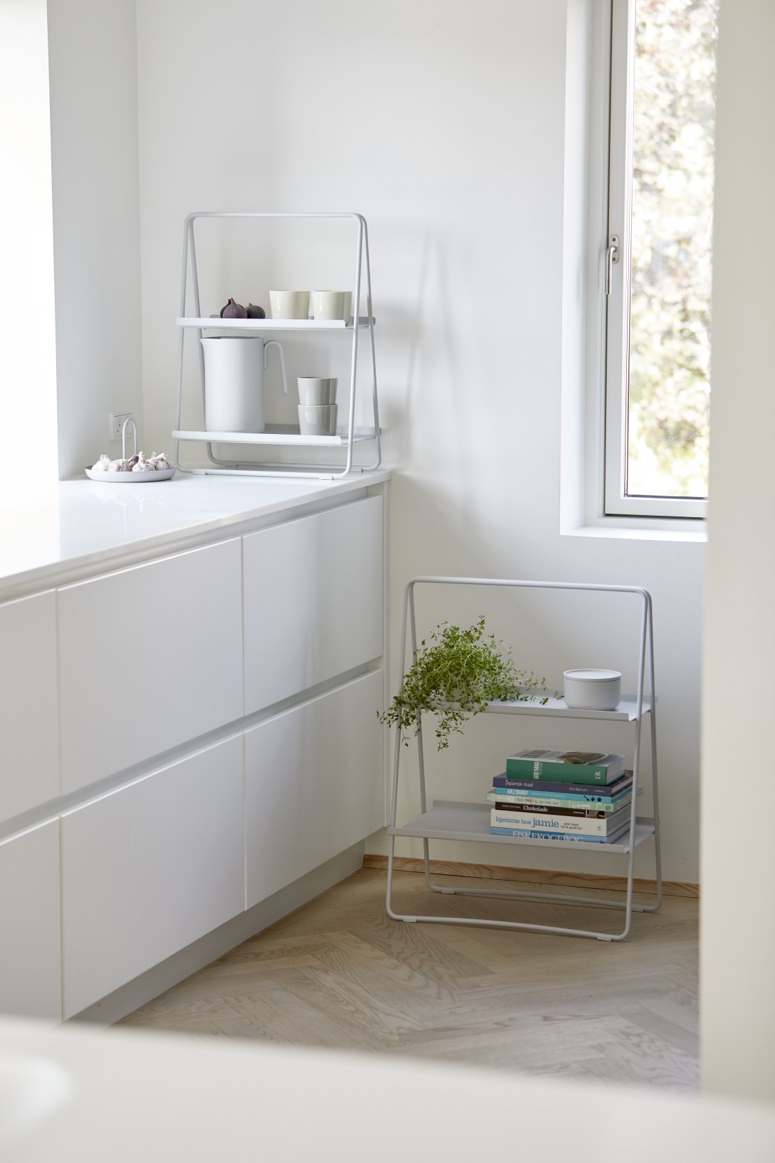 Helles Interieur mit zwei grauen A-Table Regalen von Zone Denmark, dekoriert mit Geschirr, Pflanzen und Büchern.