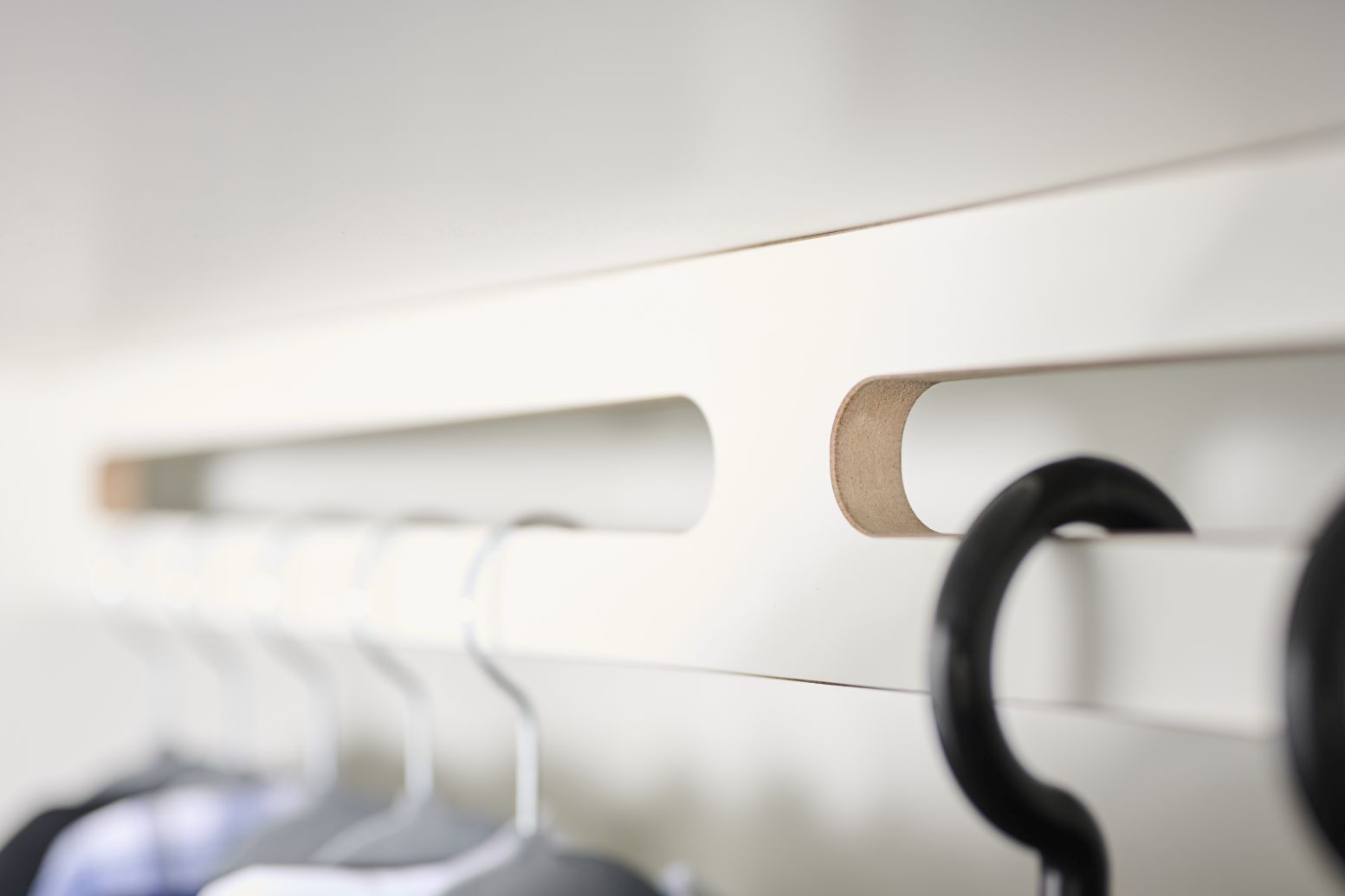 Detailaufnahme des Tojo-Schrank Grundmoduls: Weiße Schrankwand mit Kleiderbügeln an einer integrierten Kleiderstange.