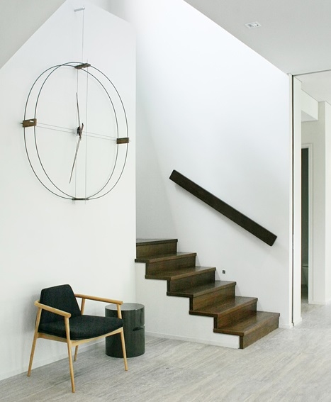 Delmori Clock Wanduhr von Nomon in modernem Interieur mit Treppe, Sessel und minimalistischem Design.