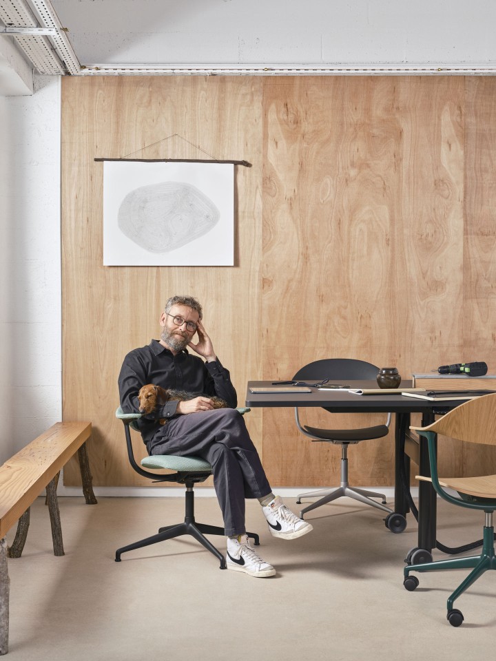 Mann mit Dackel sitzt auf einem grünen Mynt Bürodrehstuhl von Vitra im modernen Büro.