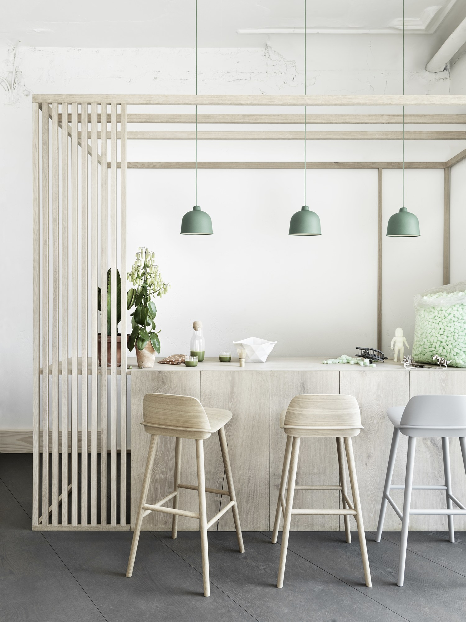 Drei grüne Muuto Grain Pendelleuchten über einer Küchentheke mit Holzhockern und dekorativen Elementen.