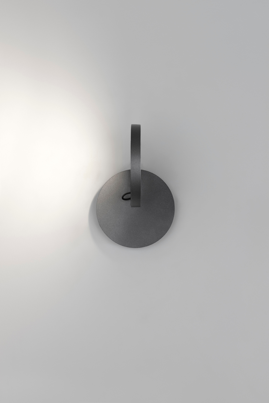 Nahaufnahme der grauen Demetra Faretto Wandleuchte von Artemide mit Schalter an einer weißen Wand.