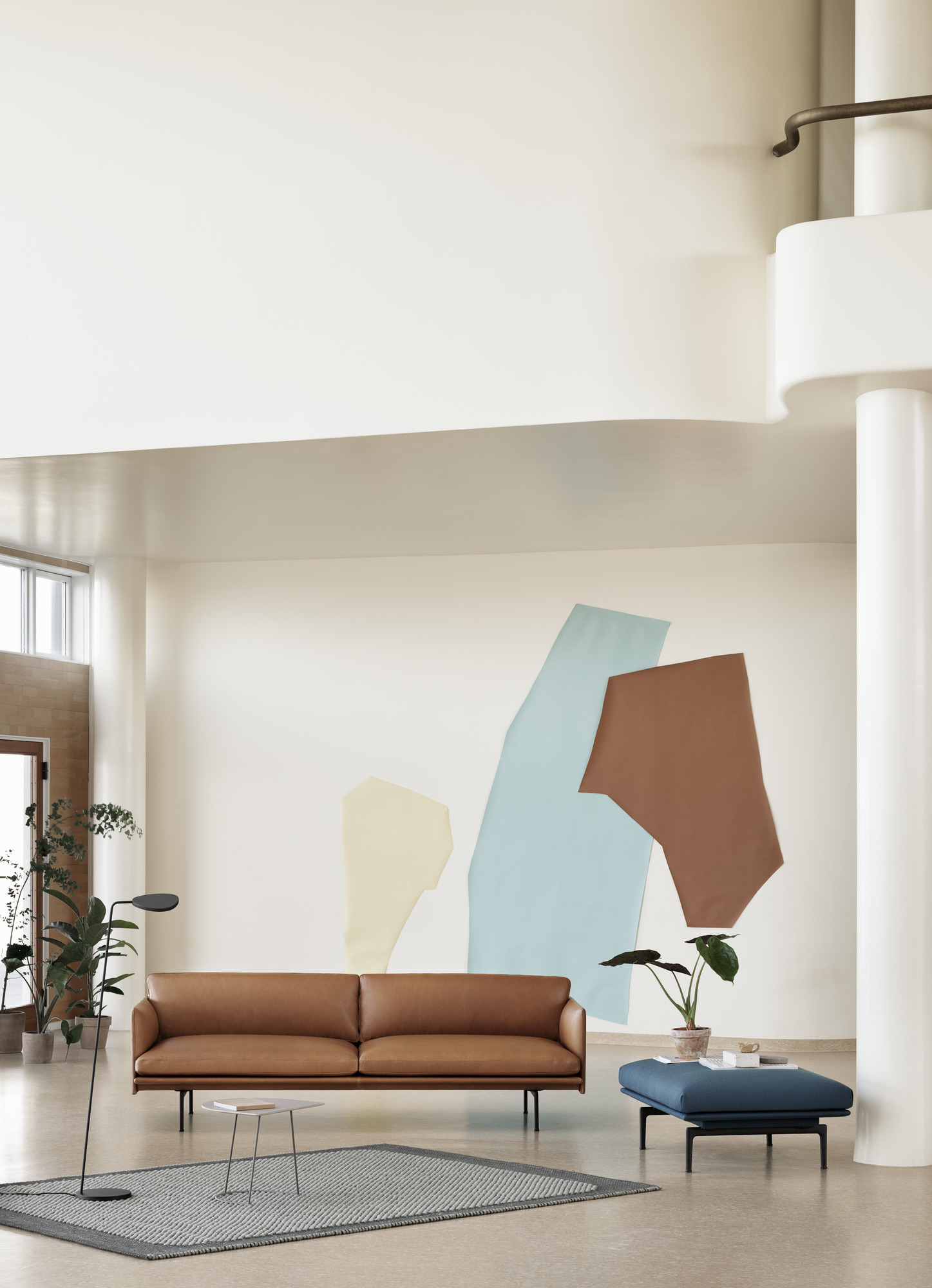 Muuto Outline Sofa, braunes Ledersofa mit passendem Hocker und Teppich in modernem Wohnzimmer.