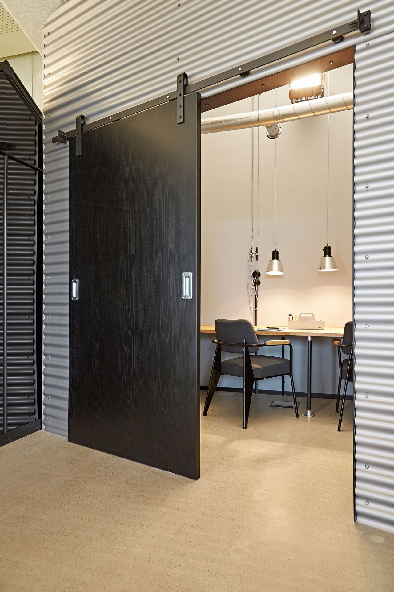 Schwarze Schiebetür aus Holz vor einem Büro mit Schreibtisch und Stühlen, modernes Design.
