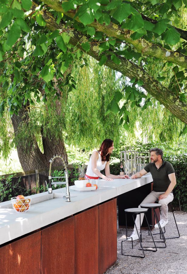Extremis Tiki Hocker: Zwei Personen sitzen an einer Outdoor-Bar auf modernen Barhockern im Garten.