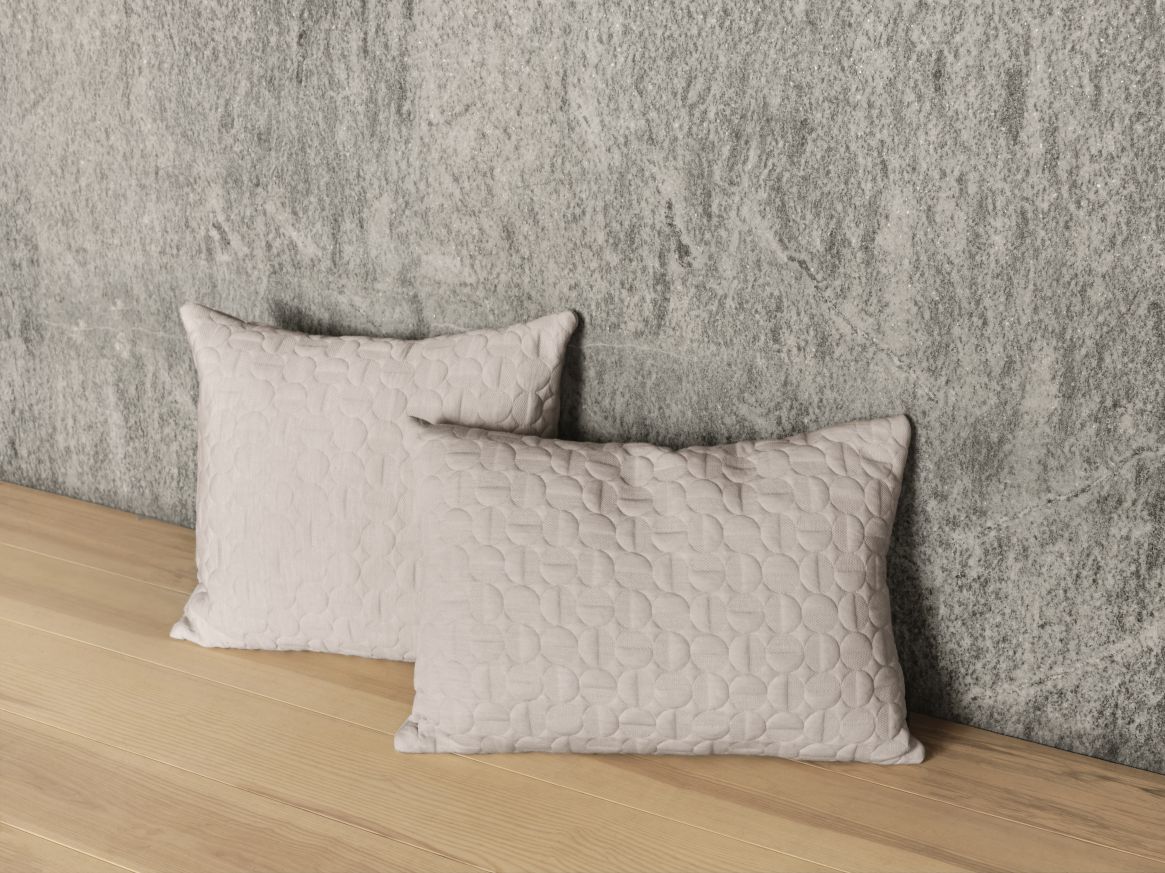 Zwei sandfarbene Arne Jacobsen Kissen von Fritz Hansen mit geometrischem Muster auf hellem Holzboden.