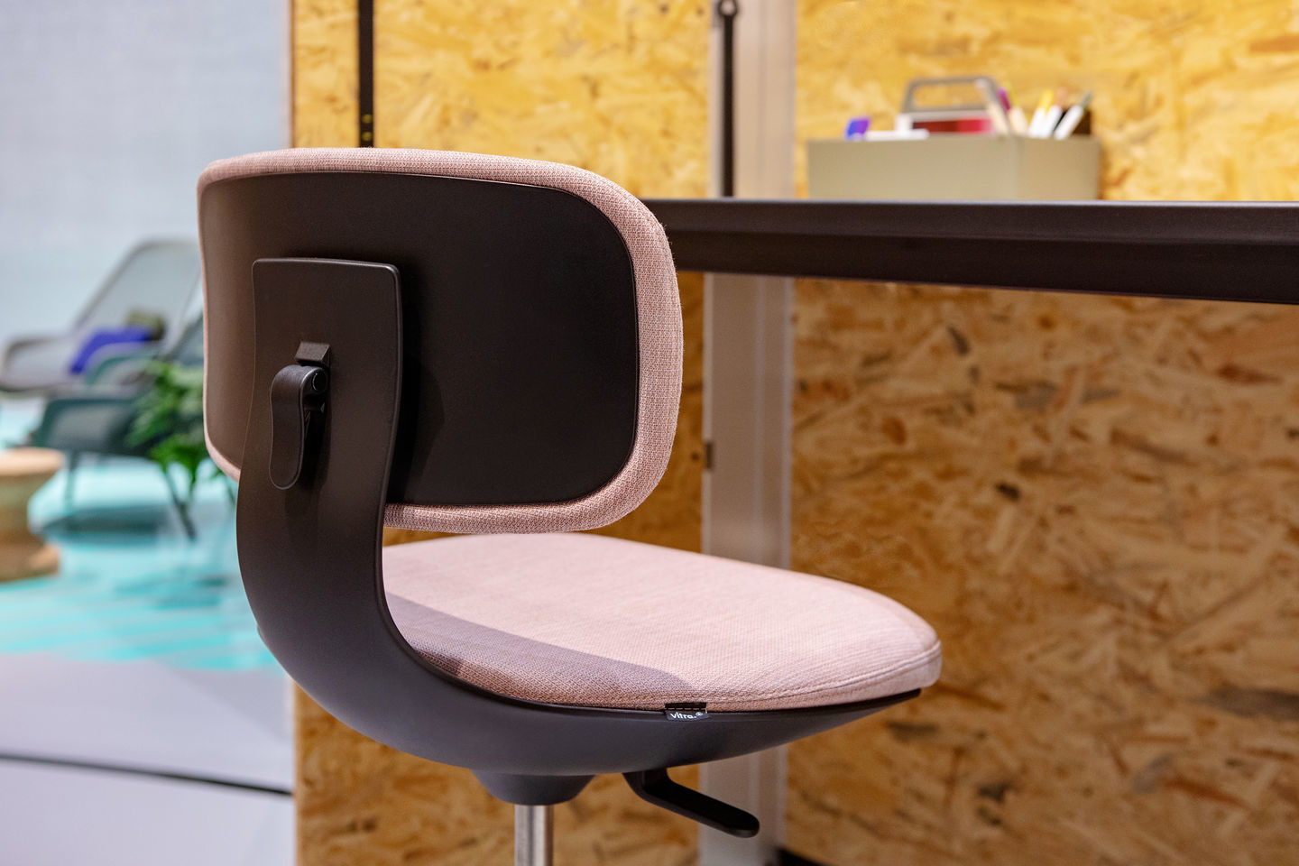 Nahaufnahme des Vitra Rookie Bürodrehstuhls mit rosa Sitzfläche und Rückenlehne vor Holzwand.