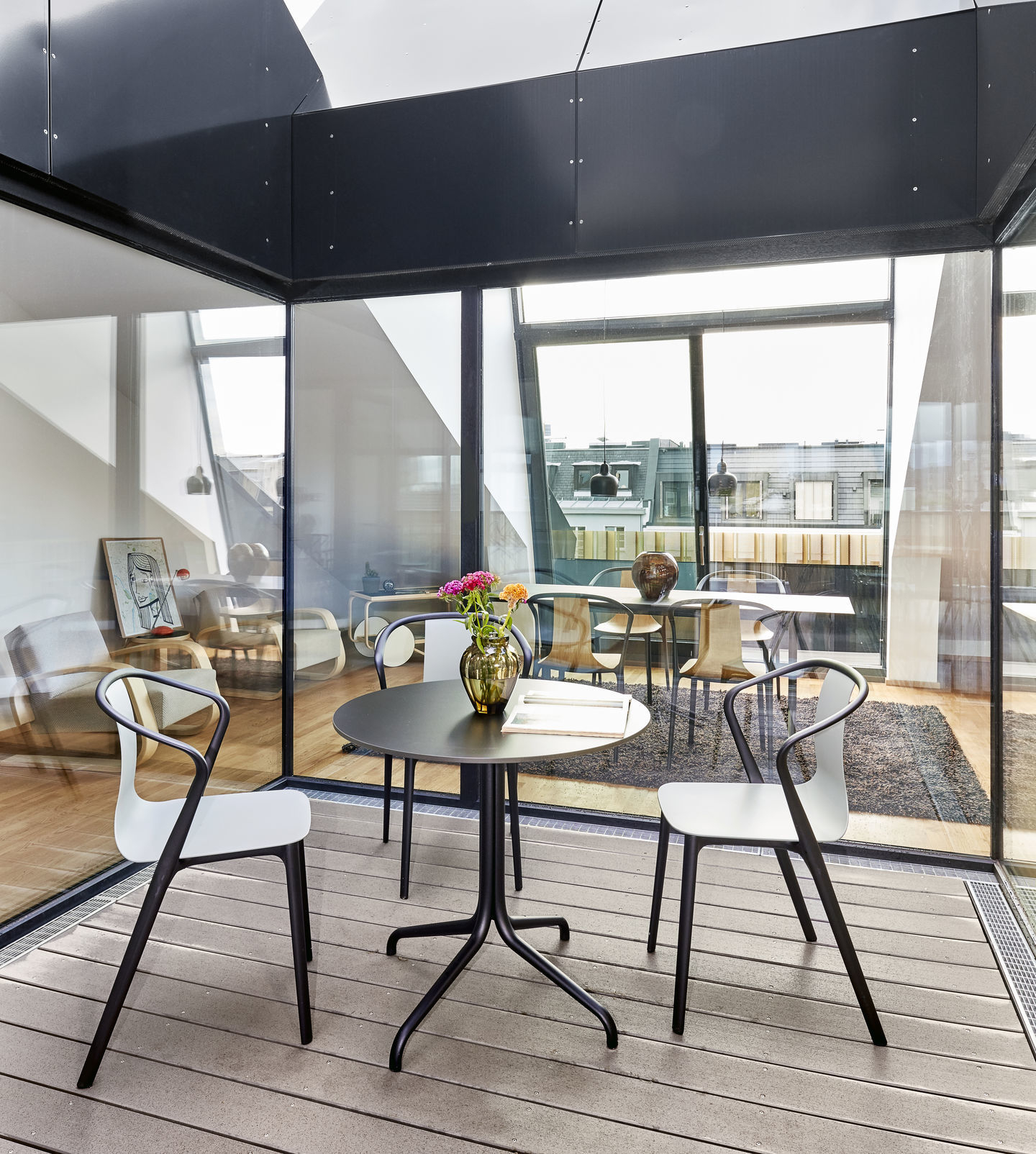 Nahaufnahme von vier Belleville Armchair Plastic Stühlen von Vitra um einen runden Tisch auf einer Terrasse.